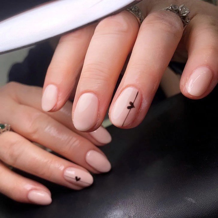 simple nude Valentines Day nails with a mini black heart nail art design accent