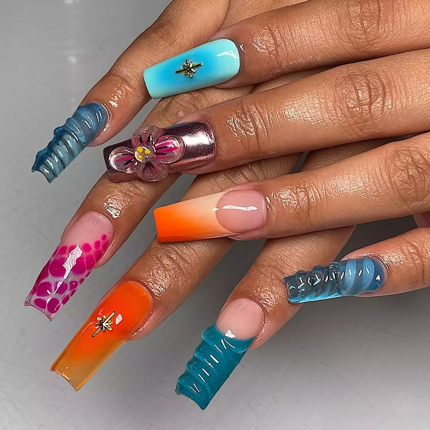 A long square manicure with 3D accents in blues, pinks, and oranges