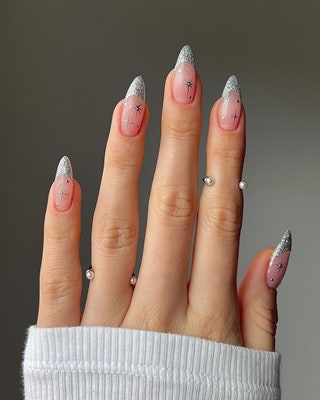 Silver glitter French tips paired with dainty snowflake nail art are festive yet understated. To create the snowflakes...