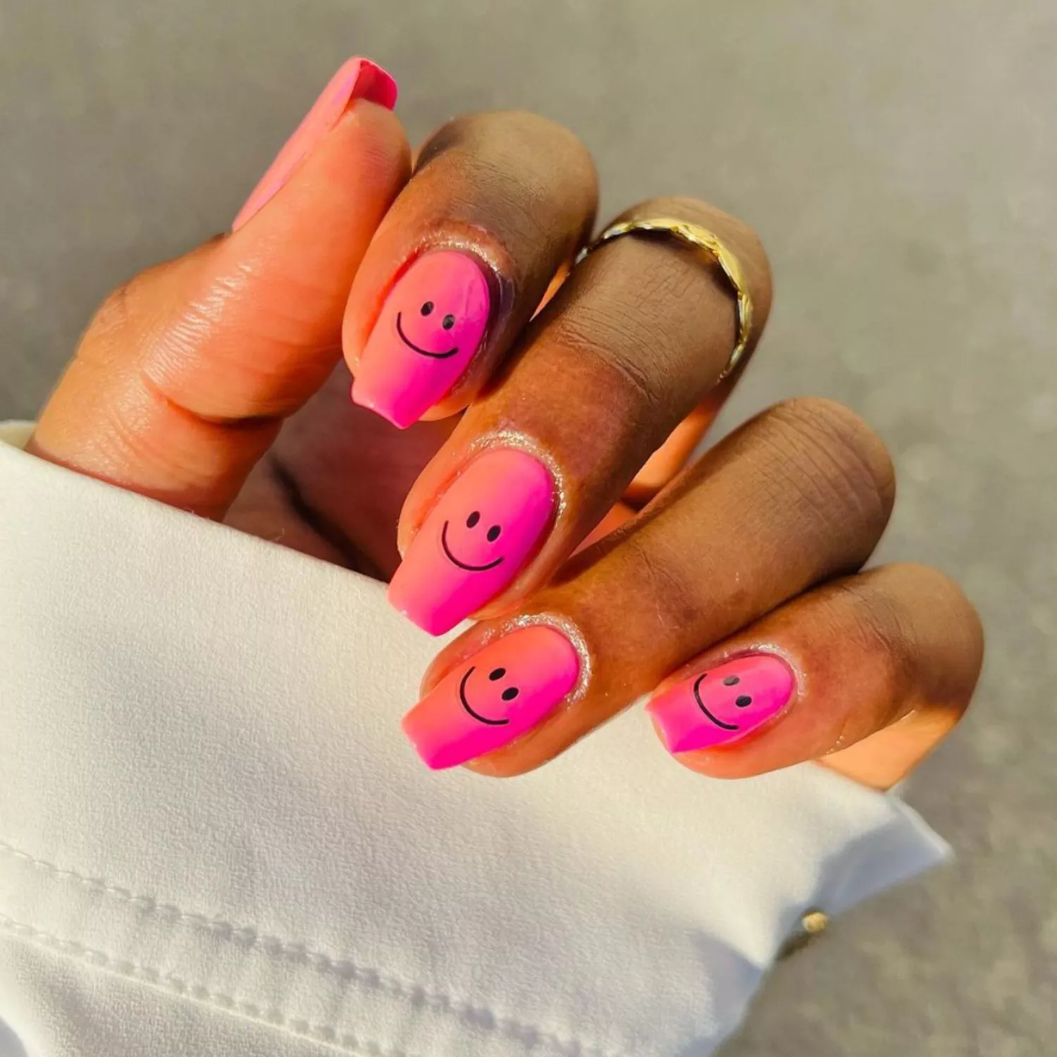 Orange to pink ombre nails with smiley faces on top.