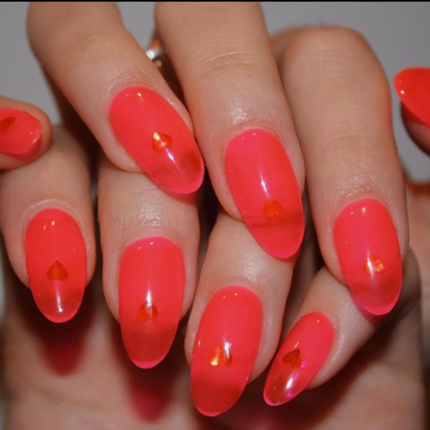 Orange-pink jelly nails with tiny heart decals.