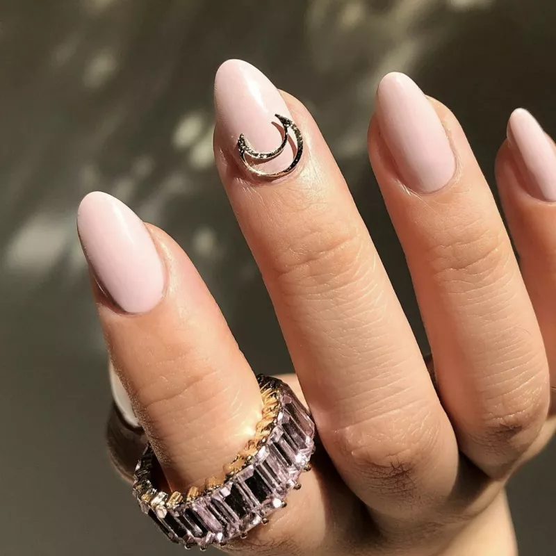 Light pink nails with a moon charm on the middle cuticle