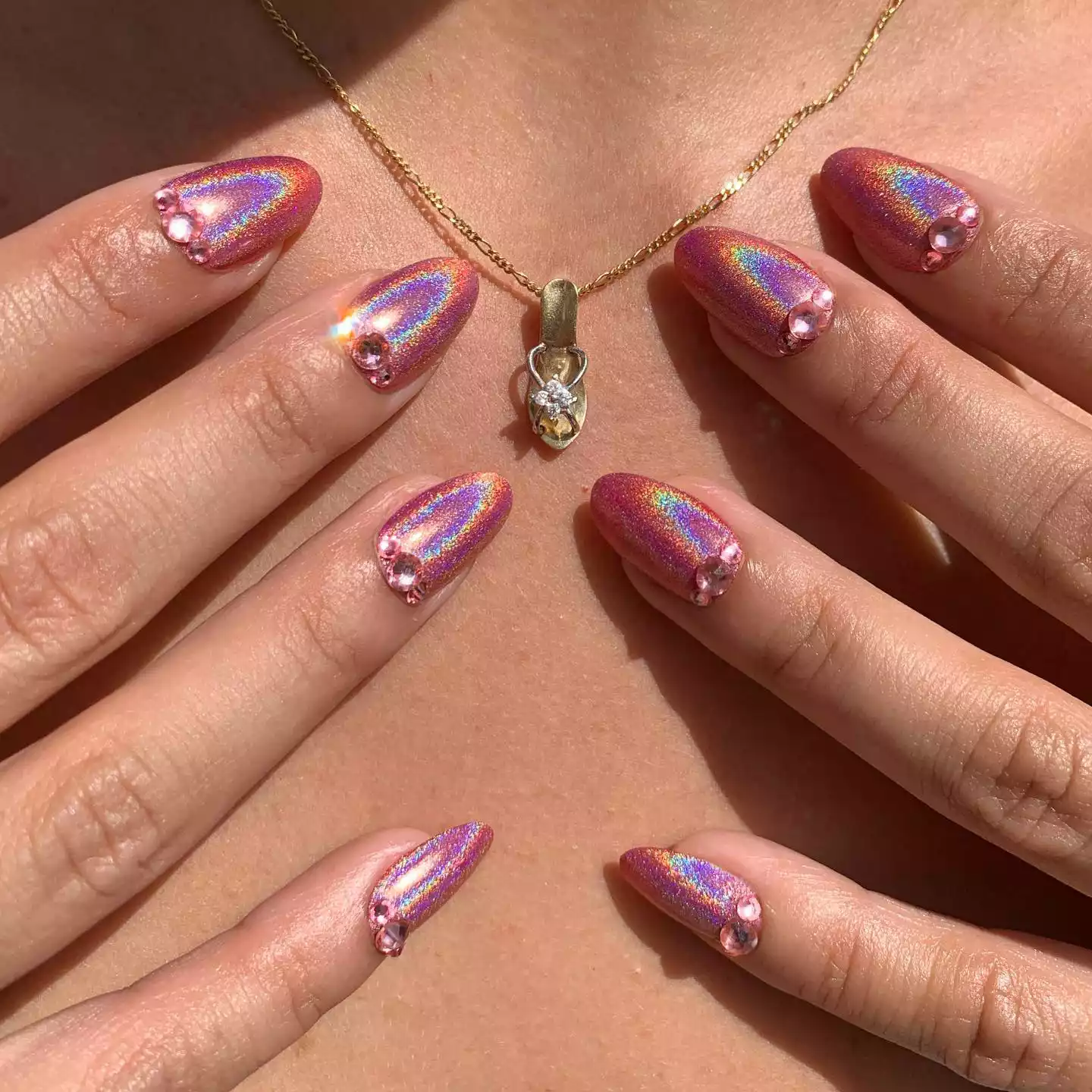 Pink iridescent nails with pink gemstones at the cuticles