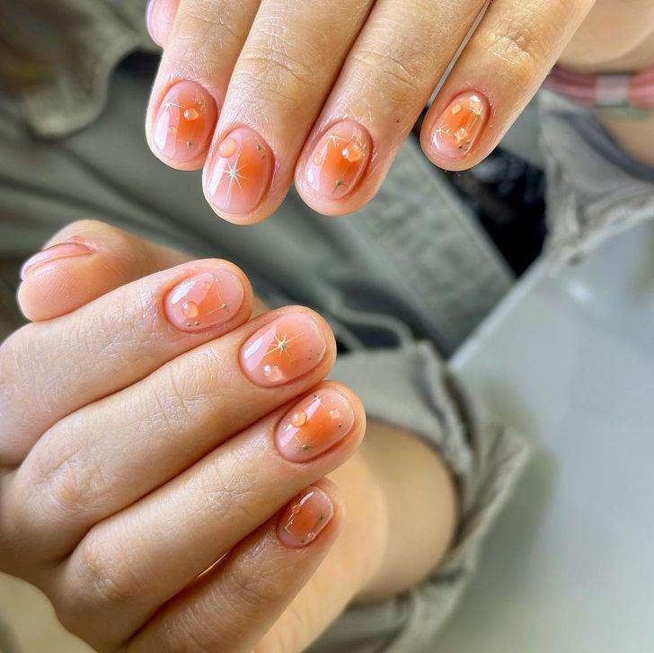 short peach orange aura nails with a gold celestial star and dot design