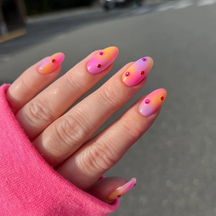 sunset inspired pink orange and purple aura nails with hot pink rhinestone design details accenting each nail