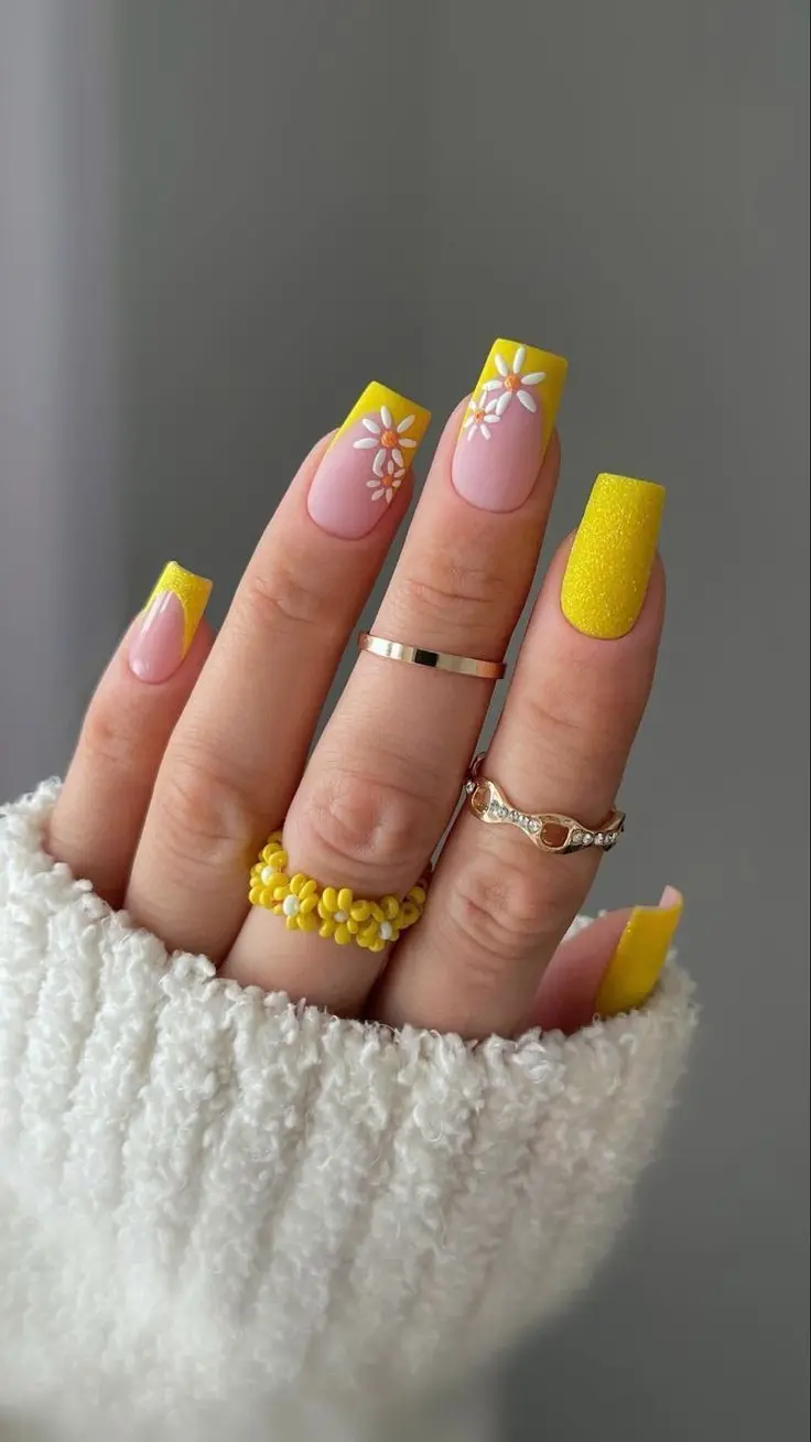 Square nails with yellow French tips, glitter accents, and delicate white and yellow floral designs. This elegant and fun summer style brings a touch of sparkle and nature-inspired beauty to your nails.