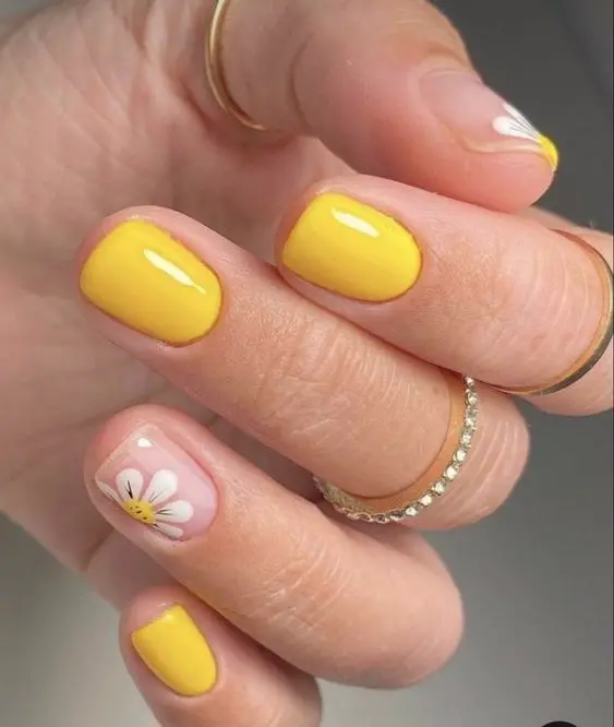 These short, squoval-shaped nails are painted in a vibrant yellow, with an accent nail featuring a simple daisy design. The combination exudes a fresh and playful summer vibe, ideal for sunny days.