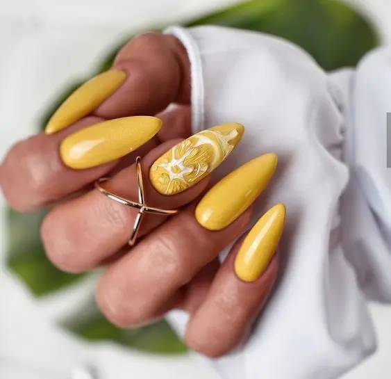 Long stiletto nails in a glossy yellow shade, with an accent nail featuring intricate white floral designs. This sophisticated style is ideal for a chic summer look.