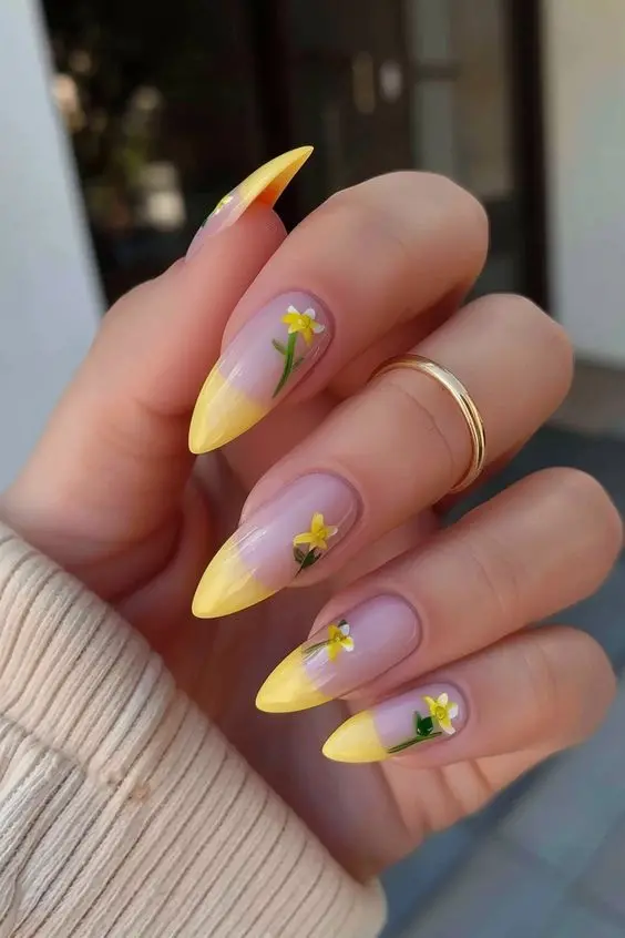 Stiletto-shaped nails with yellow French tips, accented by small yellow flowers. This sophisticated and fresh design is ideal for a sunny summer vibe.