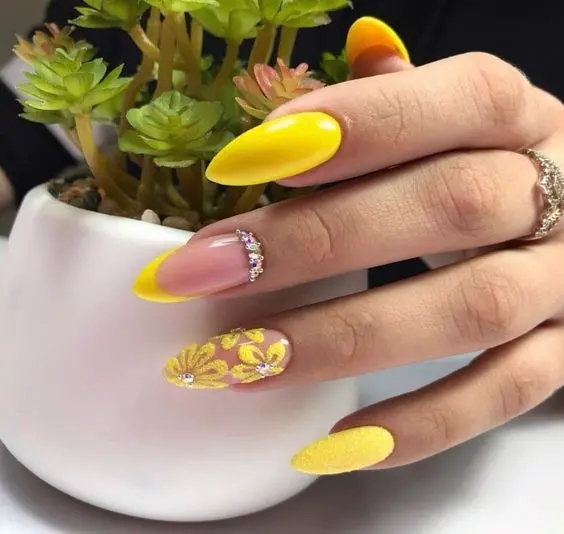 Stiletto-shaped nails with yellow French tips, accented with rhinestones and floral designs. This elegant and eye-catching style is perfect for a sophisticated summer look.