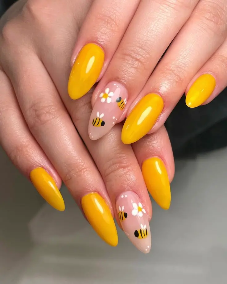 Stiletto-shaped nails in vibrant yellow with accent nails featuring daisies and bees. This playful and lively design is perfect for a fun and sunny summer day.