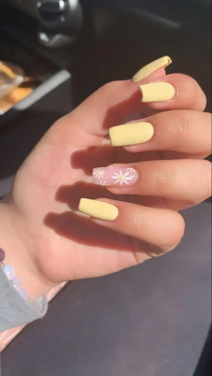 Square nails in a soft yellow shade, with a pink accent nail decorated with white daisies. This delicate and charming look is ideal for a fresh and breezy summer feel.