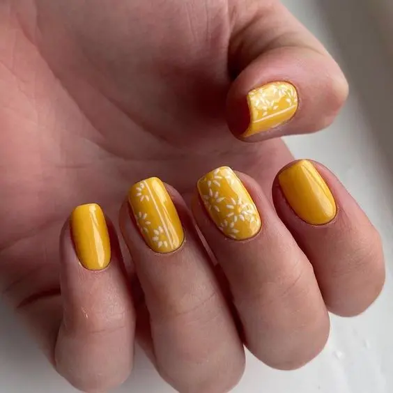 A classic set of square yellow nails, adorned with simple white floral patterns on two nails. This elegant design is perfect for a bright and cheerful summer appearance.