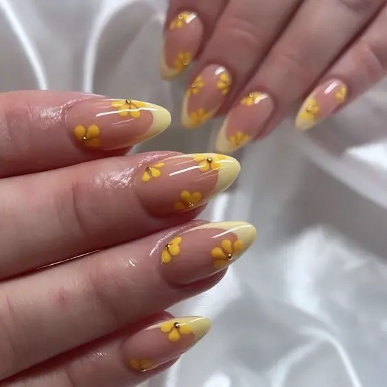 Stiletto-shaped nails with a clear base and yellow tips, adorned with small yellow flowers. This delicate and floral design is perfect for a light and airy summer look.