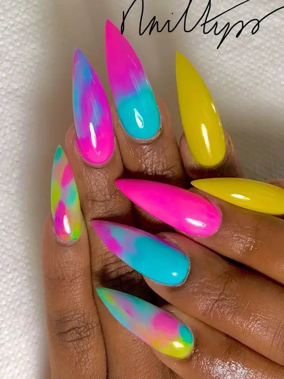 These nails feature a unique neon rainbow ombre effect with a blend of pink, blue, yellow, and green on stiletto-shaped nails. The seamless gradient and sharp nail tips exude a fierce and trendy vibe, perfect for those looking to showcase their edgy and creative side.