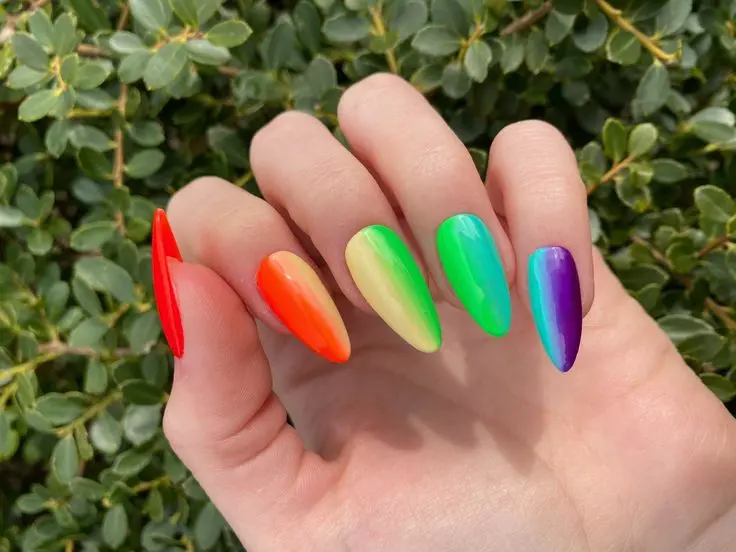 These stiletto-shaped nails showcase a glossy neon rainbow gradient, transitioning from red to purple. The bright and cheerful colors create a fun and lively look, perfect for someone who loves to express their vibrant personality.