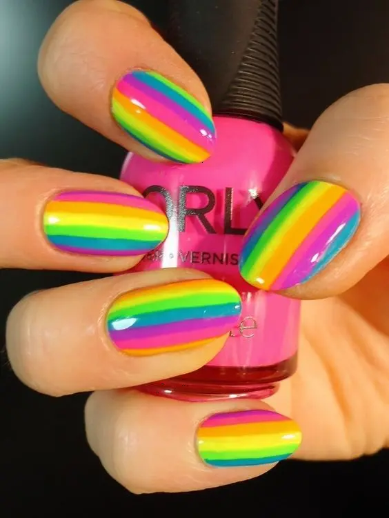 This vibrant look features rounded shaped nails with horizontal stripes in neon rainbow colors. Each stripe is perfectly aligned to create a continuous rainbow effect, making them a dazzling choice for those looking to stand out.