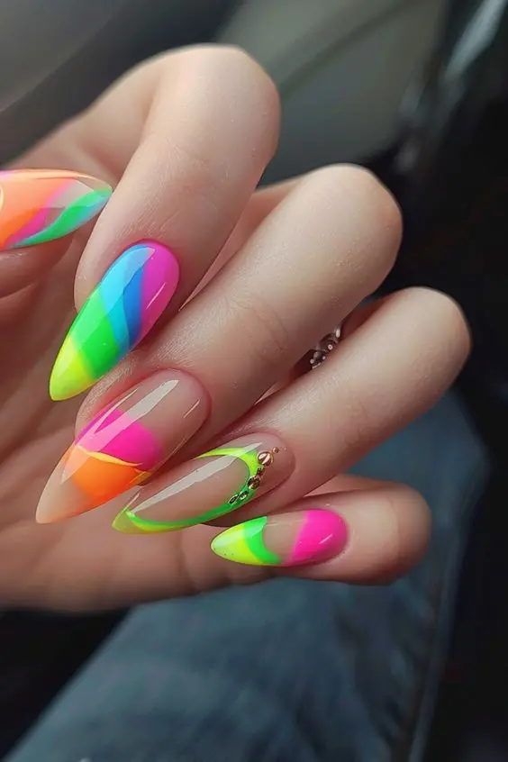 Long, stiletto-shaped nails are adorned with neon rainbow diagonal stripes, highlighted with rhinestones on a nude base. The combination of bright colors and sparkling accents creates a chic and glamorous look, perfect for adding a touch of luxury to any outfit.