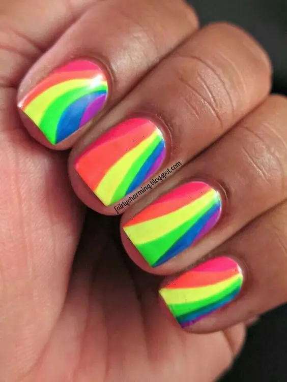 These neon rainbow nails feature curving stripes of bright colors, including pink, orange, green, and blue, on a square nail form. The harmonious blend of hues gives a playful and dynamic vibe, ideal for someone looking to add a pop of color and excitement to their look.