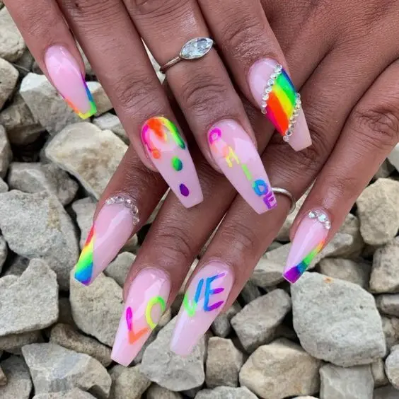 These long ballerina nails feature a romantic theme with neon rainbow accents, \'LOVE\' lettering, and subtle embellishments. The design combines soft pastel pink with bright rainbow colors, creating a unique, love-inspired look adorned with rhinestones for added sparkle.