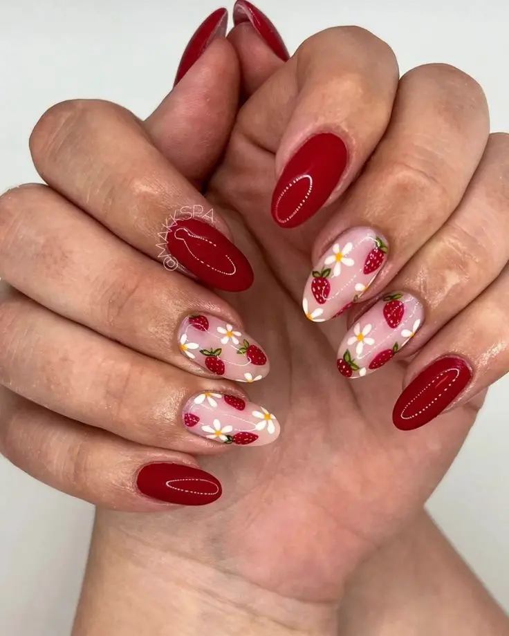 Showcasing a mix of glossy red and strawberry patterned designs, this manicure uses almond-shaped nails to create a playful yet elegant look. The intricate strawberries and small white flowers are set against a transparent background, emphasizing simplicity and freshness.