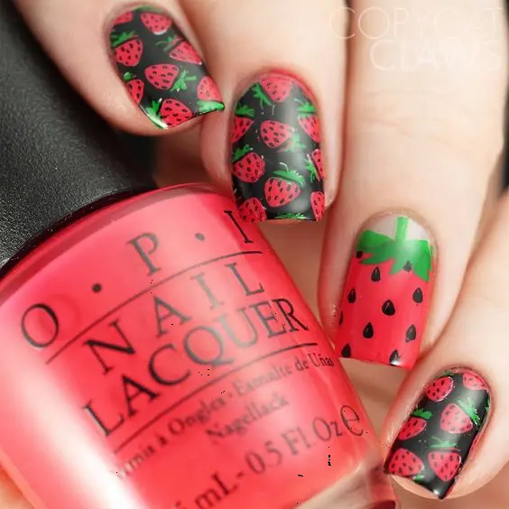 The manicure showcases deep green nails with black accents, adorned with red strawberry prints, offering a unique twist on the classic fruit theme. Perfect for those seeking a distinctive yet stylish nail art.