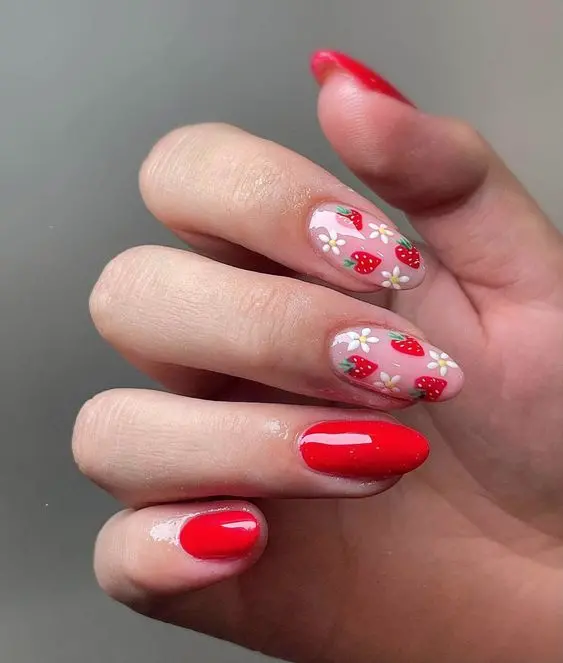 This vibrant nail design features bright red almond-shaped nails, with several nails adorned with cute strawberry and white flower patterns on a sheer base. The bold red color contrasts beautifully with the delicate floral design, perfect for a summer look.