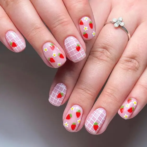 This manicure features soft pink squoval nails with a white grid pattern and scattered strawberry and flower motifs. The design combines simplicity with charm, offering a playful yet sophisticated look suitable for spring and summer.