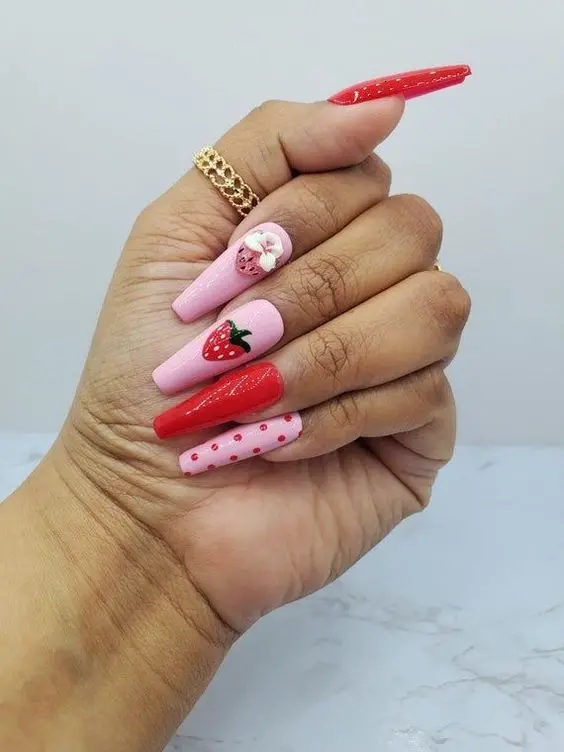 This vibrant manicure features long ballerina nails in a mix of bold red and soft pink, with polka dots and detailed strawberry designs. The striking color combination and playful embellishments make this a standout choice for fashion-forward nail enthusiasts.