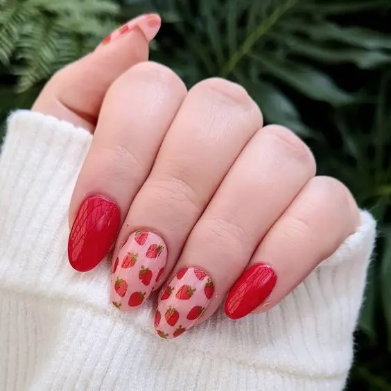 This manicure pairs bold red rounded-shaped nails with others showcasing delicate strawberry illustrations on a soft pink base. The design is modern yet timeless, suitable for those who love a pop of color.