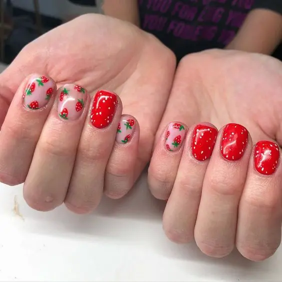 Squoval nails with glossy red and strawberry designs create a fun, vibrant look. This manicure is perfect for anyone wanting to add a playful yet elegant touch to their style.