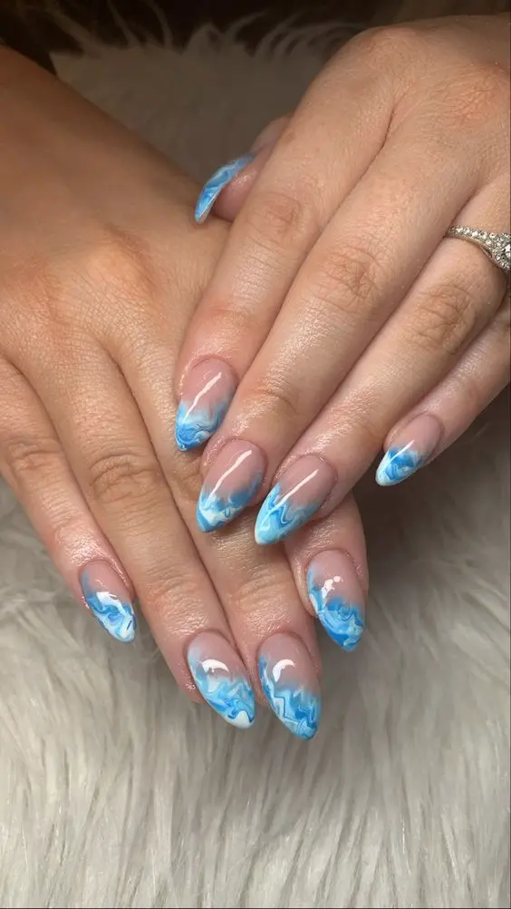 This summer beach nail design features stiletto-shaped nails with a natural base and blue marble waves at the tips. The seamless blend of blues and whites evokes the essence of ocean waves, perfect for a summer beach look.