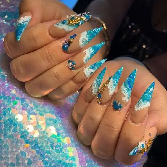 These nails feature a stiletto form with intricate beach waves and golden seashell accents. The vibrant blue and white colors create a stunning oceanic look, perfect for summer beach vibes.