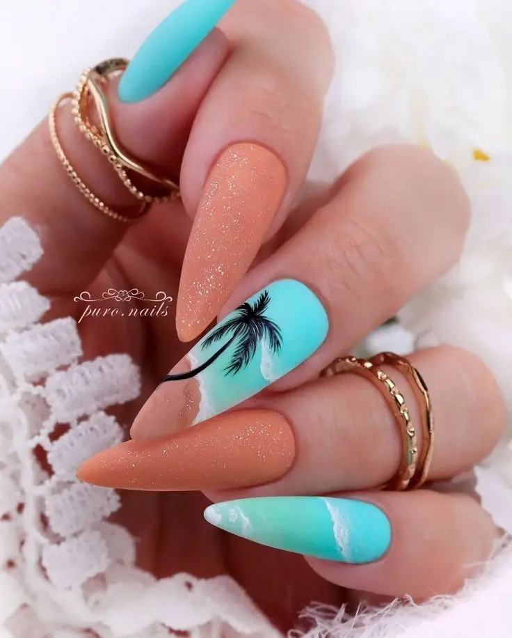 These stiletto-shaped nails blend sandy peach and turquoise colors, accented with palm tree silhouettes. The matte finish and glitter add a touch of glamour, making them perfect for a tropical summer.