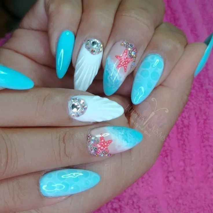 Stiletto-shaped nails with a mix of bright blue, white, and intricate starfish and shell embellishments. This playful and vibrant design brings a piece of the beach to your fingertips, making it a fun summer accessory.