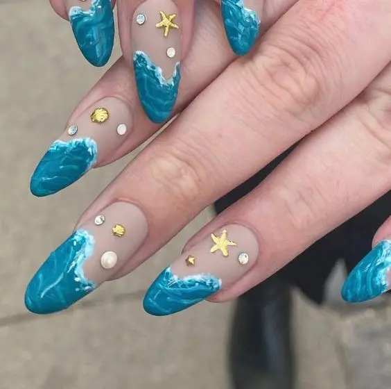 Almond nails with vibrant blue waves and gold starfish accents. The combination of deep blue and shimmering gold captures the essence of a sunny beach day.