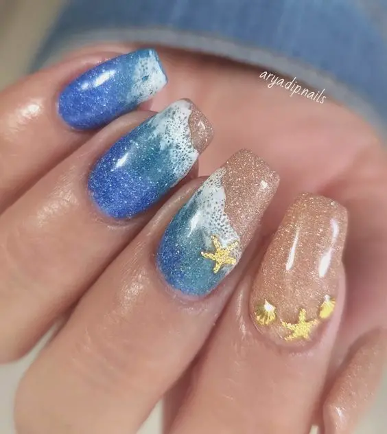 Ballerina-shaped nails with blue waves and sandy glitter accents. The sparkling details and oceanic theme capture the essence of a sunny beach day.