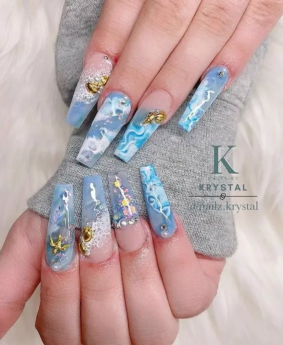 Ballerina-shaped nails featuring blue and white waves with gold accents and jewels. The intricate design embodies the beauty and mystique of the ocean, perfect for summer.