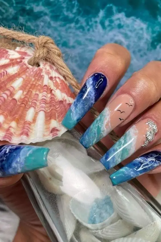 Long ballerina-shaped nails with blue and white wave patterns, featuring seagull silhouettes. This design captures the calm and breezy essence of a summer beach day.