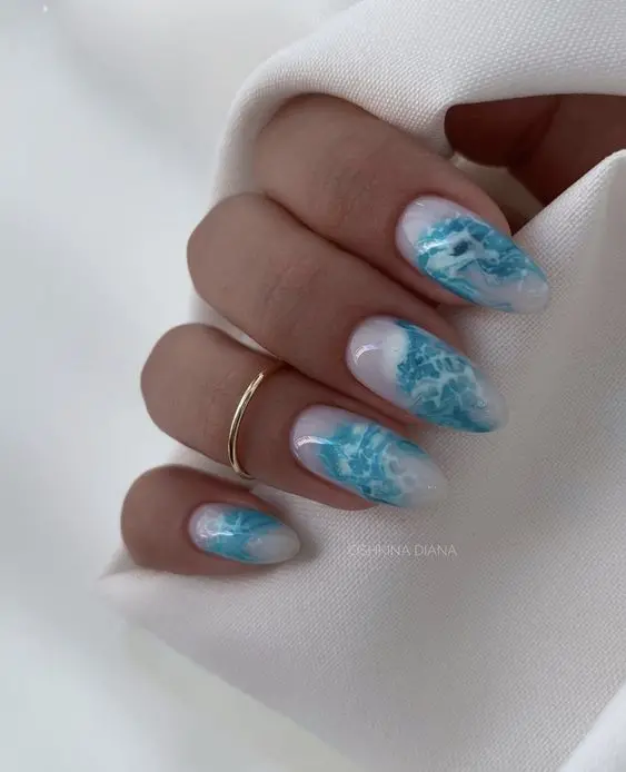 These nails have a medium almond shape with a gradient blue and white design. The subtle, delicate waves create an elegant and sophisticated look, ideal for summer events. The soft colors and fluid patterns emphasize a serene beach atmosphere.