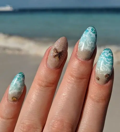 Almond-shaped nails with sandy beige and blue wave designs, accented by starfish and seashells, evoke a serene beach atmosphere perfect for summer.