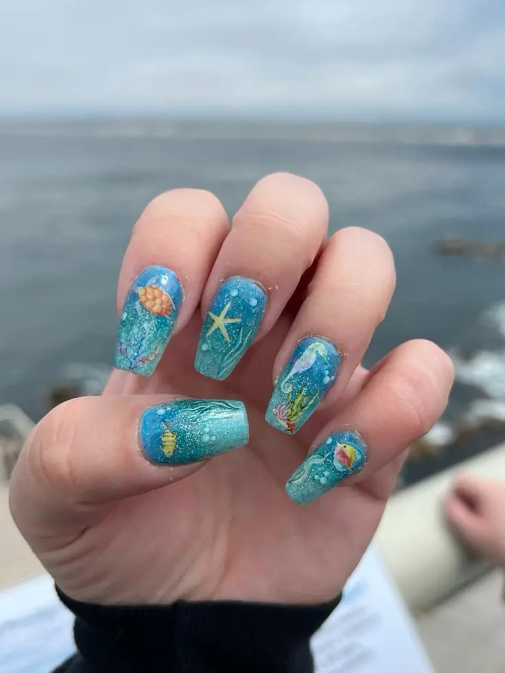 Ballerina-shaped nails with detailed sea life and ocean scenery in blue and green hues. This design evokes the magical experience of exploring underwater worlds during summer.