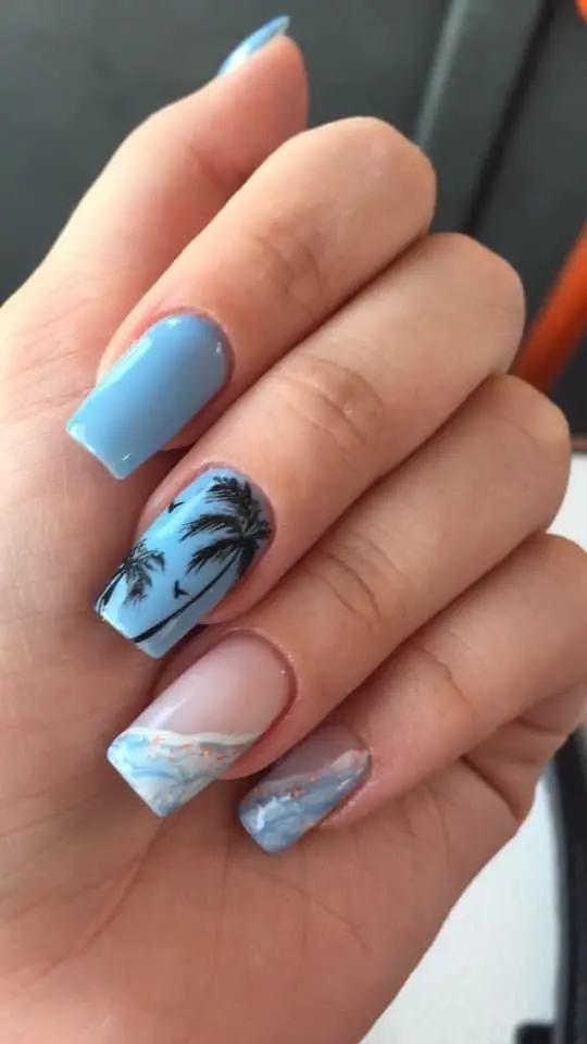 The square nails feature a gradient effect from blue to turquoise, adorned with palm trees and ocean waves. This intricate design captures the vibrant and playful spirit of summer.