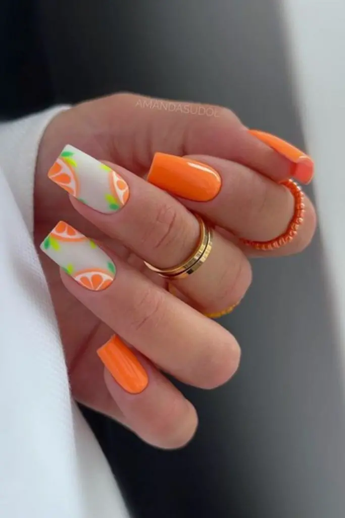 Long, square nails in a vivid orange hue are complemented by white nail tips with citrus wedge designs, offering a bright, summery manicure.