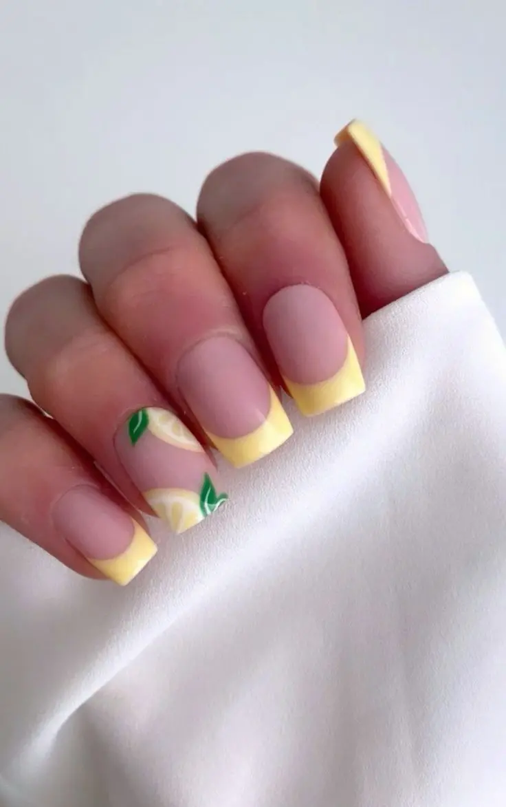 Sheer pink nails with sunny yellow tips and lemon accents offer a refreshing twist on the classic French manicure, ideal for summer.