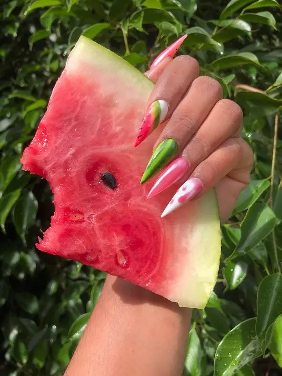 These stiletto nails combine a gradient of pink and green with a watermelon design, creating a fresh, summery look with a sharp edge.