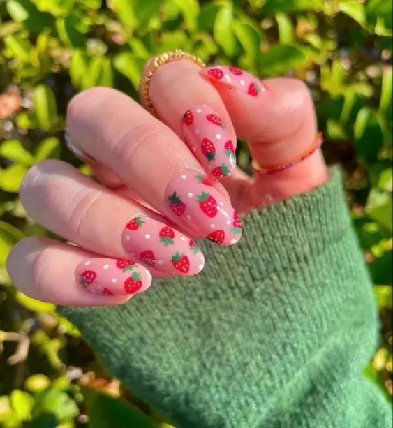 Summer-ready nails with a sheer base, sprinkled with charming strawberry patterns and tiny green leaves, capturing the essence of a sunny fruit garden.