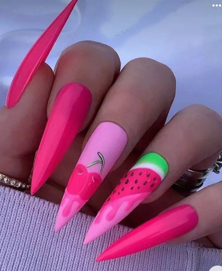 Sharp, stiletto nails painted in a hot pink gradient with playful watermelon designs on alternating nails offer a fresh, fruity summer style.