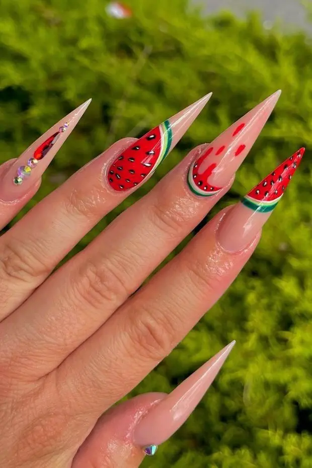 A vibrant manicure with stiletto nails, each showcasing a glossy red base and detailed watermelon design, ideal for summer festivities.