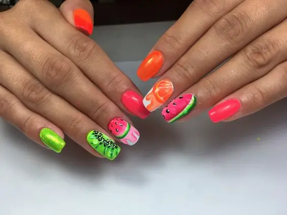 A bold, fun mix of neon green and hot pink, with nails displaying various fruit patterns, including watermelon and orange, for a playful summer statement.